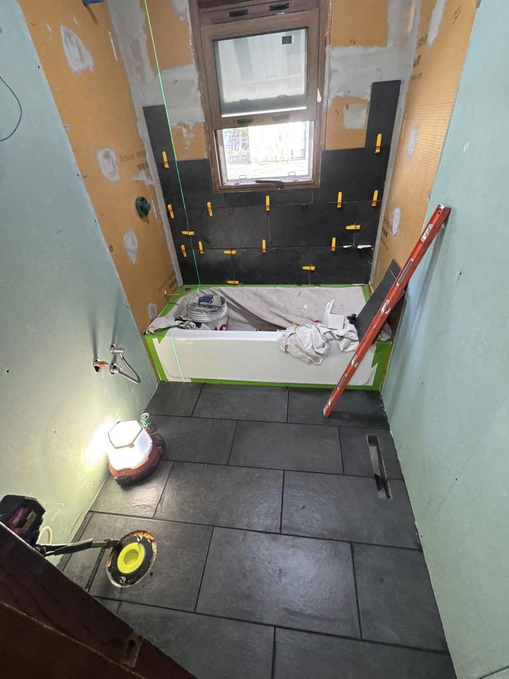 Dark slate tile floor laid and tub set, walls being tiled