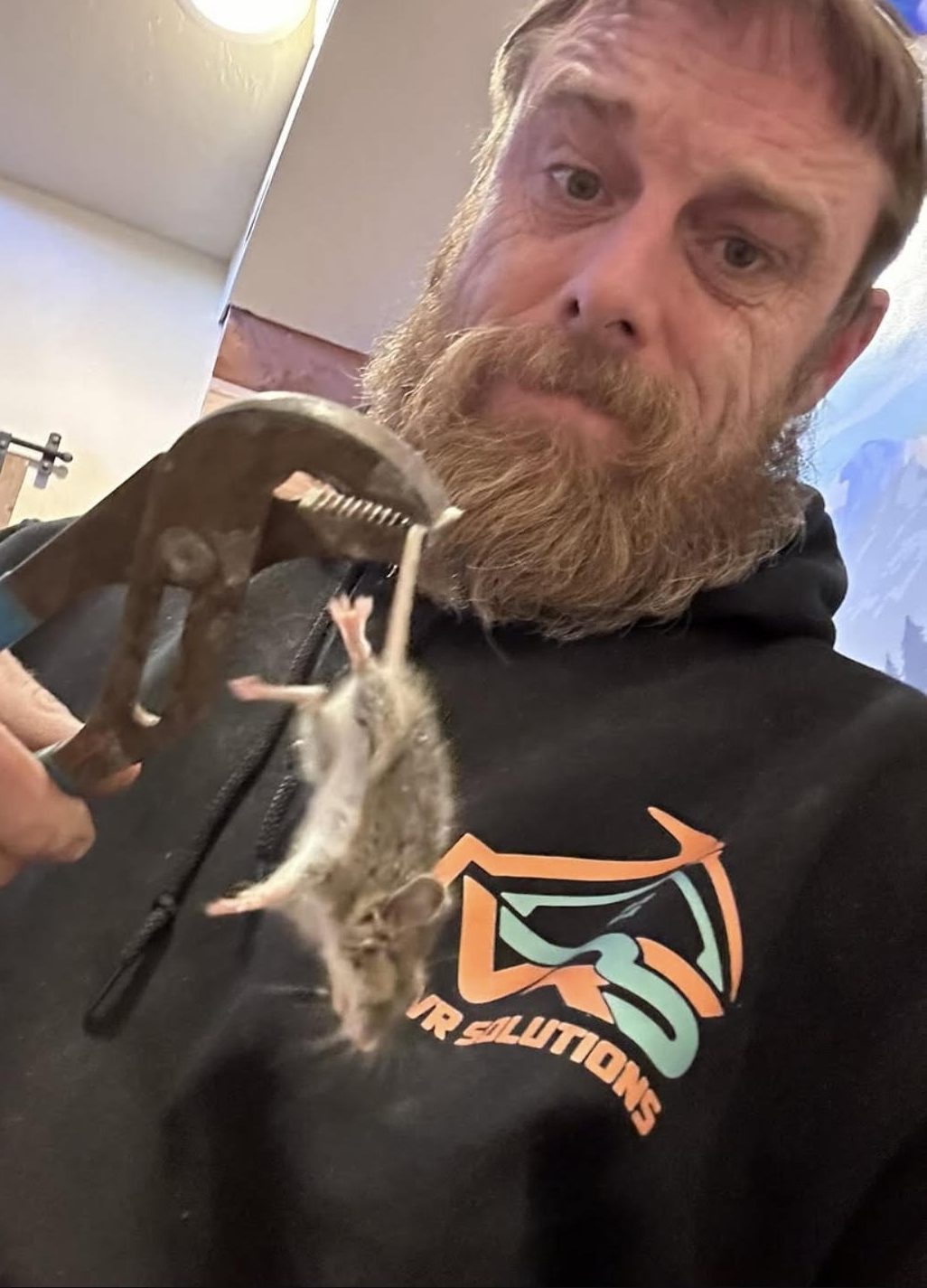Aaron of VR Solutions holding a mouse with a pair of channel-lock pliers, wearing a VR Solutions hoodie