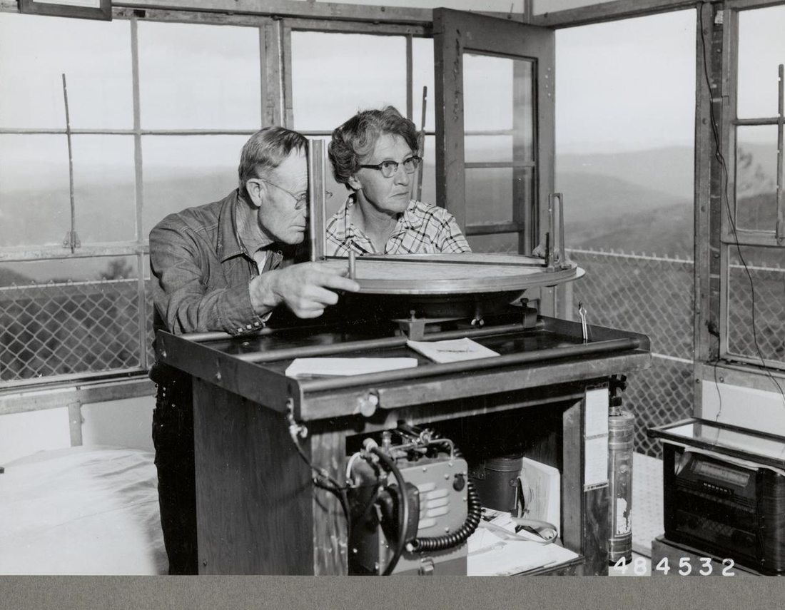 Two fire lookouts using an alidade in a San Juan National Forest fire tower in 1957
