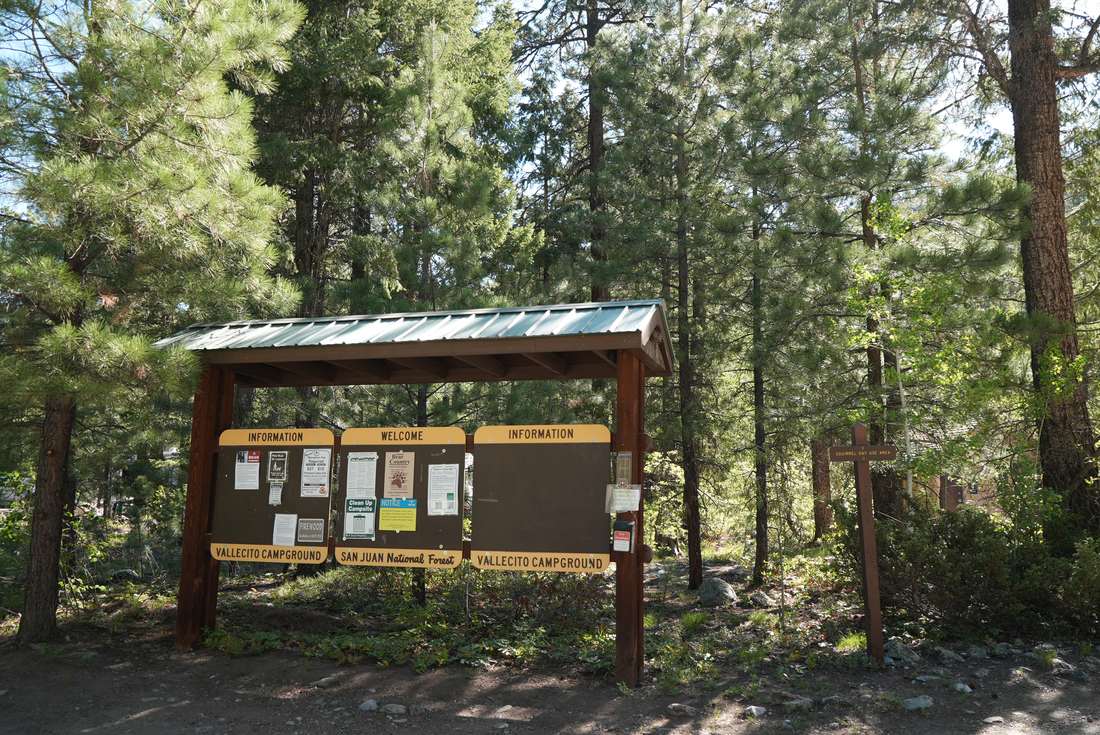 The wooden Vallecito Campground welcome and information board in the pines, lettered San Juan National Forest