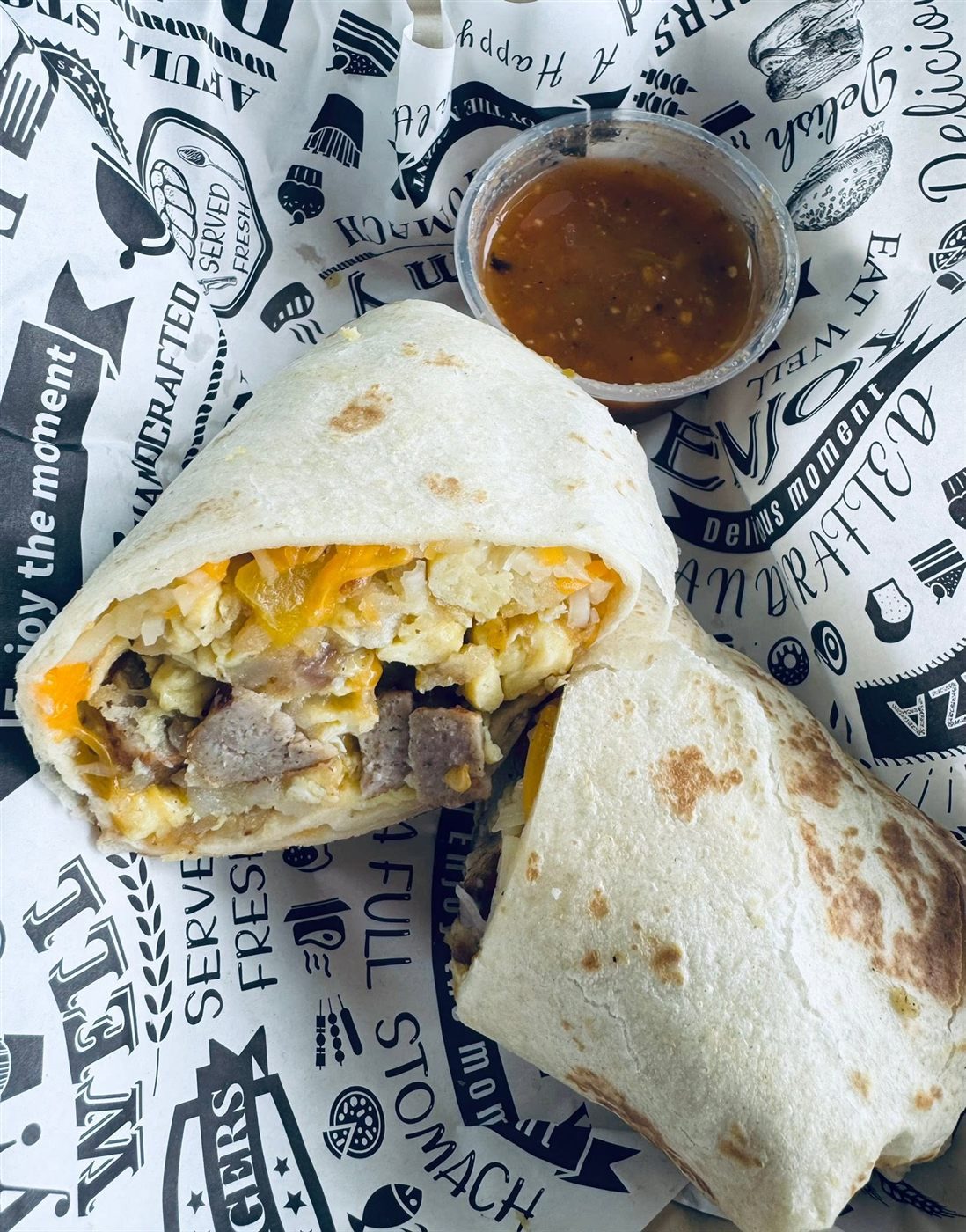 A breakfast burrito cut in half to show the egg, cheese and sausage inside